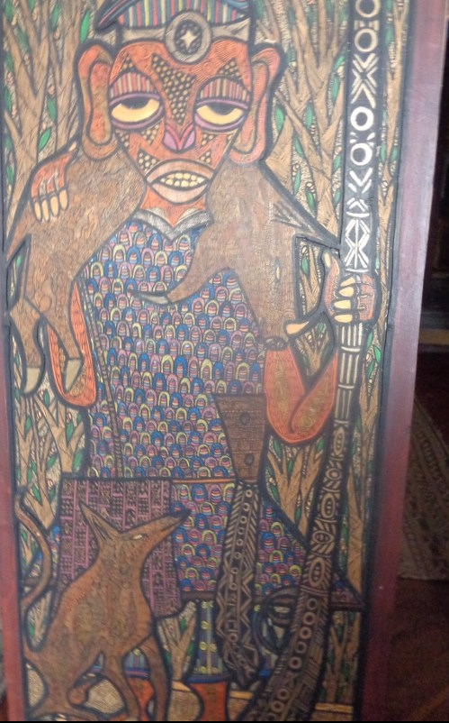 A work of art by the late Twins Seven Seven, who was noted for his intricate doodles on wood, done with pen and ink and crayon. It shows a hunter with his kill and gun. The most flamboyant of the “Oshogbo” artists, Twins has had an enormous impression on younger artists and the New York Times ran a long obituary on his life when he died in 2011.